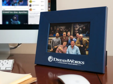 Blue tabletop photo frame with DreamWorks Animation Television logo, displaying a group photo of smiling employees in an office setting.