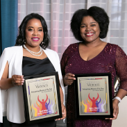 Two women dressed in formal attire holding framed “Enterprising Women of the Year” award plaques, smiling at an event.